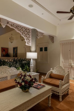 A room with a white ornate sofa, a matching armchair, a coffee table with a vase of flowers, and a white cabinet. - Justa Luxe Kashi Parampara, Varanasi (Varanasi)