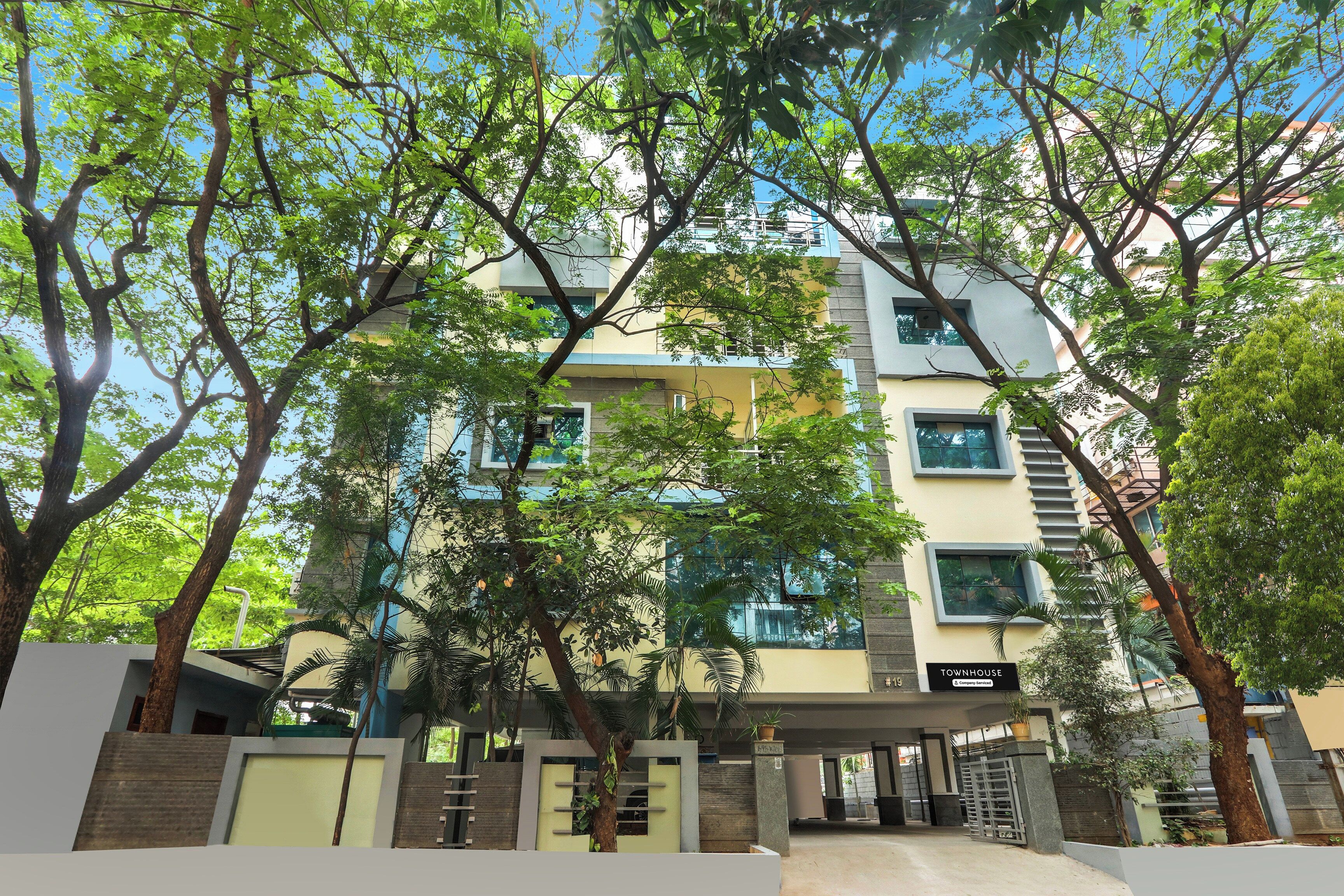 Un edificio de varios pisos con un acceso cubierto, rodeado de árboles.