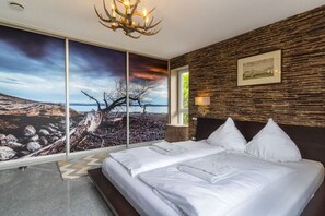 A bedroom with a large bed, a chandelier, a view of a landscape through a window, and a textured wall. - Holiday apartment with 1 bedroom (Gaienhofen)