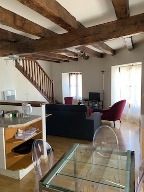 A living room with a glass coffee table, wooden beams on the ceiling, a staircase, and a red chair. - New Listing (Pleaux)