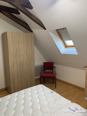 A room with a sloped ceiling, a skylight, a wooden wardrobe, a red chair, and a mattress. - New Listing (Pleaux)