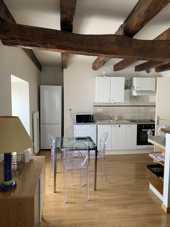 A modern kitchen with wooden beams, white cabinets, a glass dining table, and clear chairs. - New Listing (Pleaux)