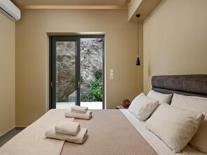 A hotel room with a bed, towels, a view of a rocky landscape through a glass door, and a pendant light. - Mitos Ultimate Escape Villa (Naxos)