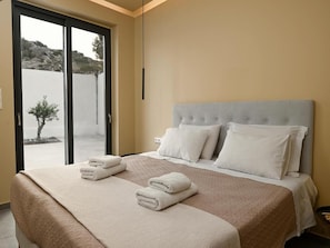 A hotel room with a bed, two pillows, a bedside table, and a view through a glass door. - Mitos Ultimate Escape Villa (Naxos)