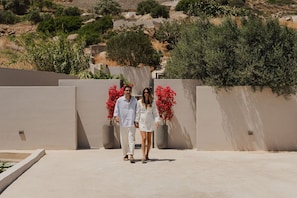 A couple walking on a flat rooftop with a view of a hilly landscape and a wall with red flowers. - Mitos Ultimate Escape Villa (Naxos)