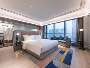 A modern hotel room with a large bed, a seating area with cushions, a view of the city through large windows, and a robe rack with towels. - Mercure Lanzhou Downtown (Lanzhou)