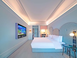 Habitació d'hotel amb un llit gran, televisió penjada a la paret, escriptori amb cadira i taula petita amb làmpada.