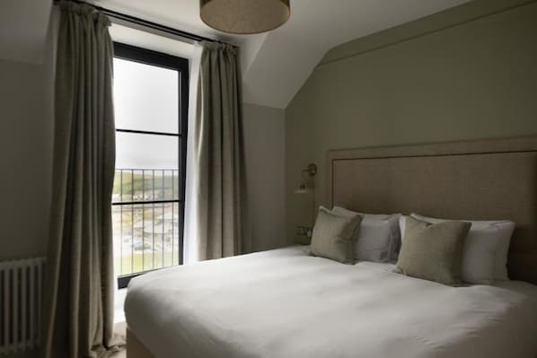 A bedroom with a large bed, a window with curtains, and a headboard. - The Edge Of The Beach (Bude)