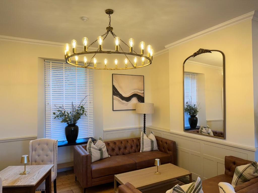 A living room with a brown sofa, a coffee table, a lamp, a chandelier, a mirror, and a painting on the wall.
