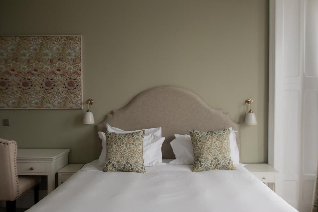 A neatly made bed with white bedding and patterned pillows, a headboard, bedside tables with lamps, and a wall-mounted artwork.