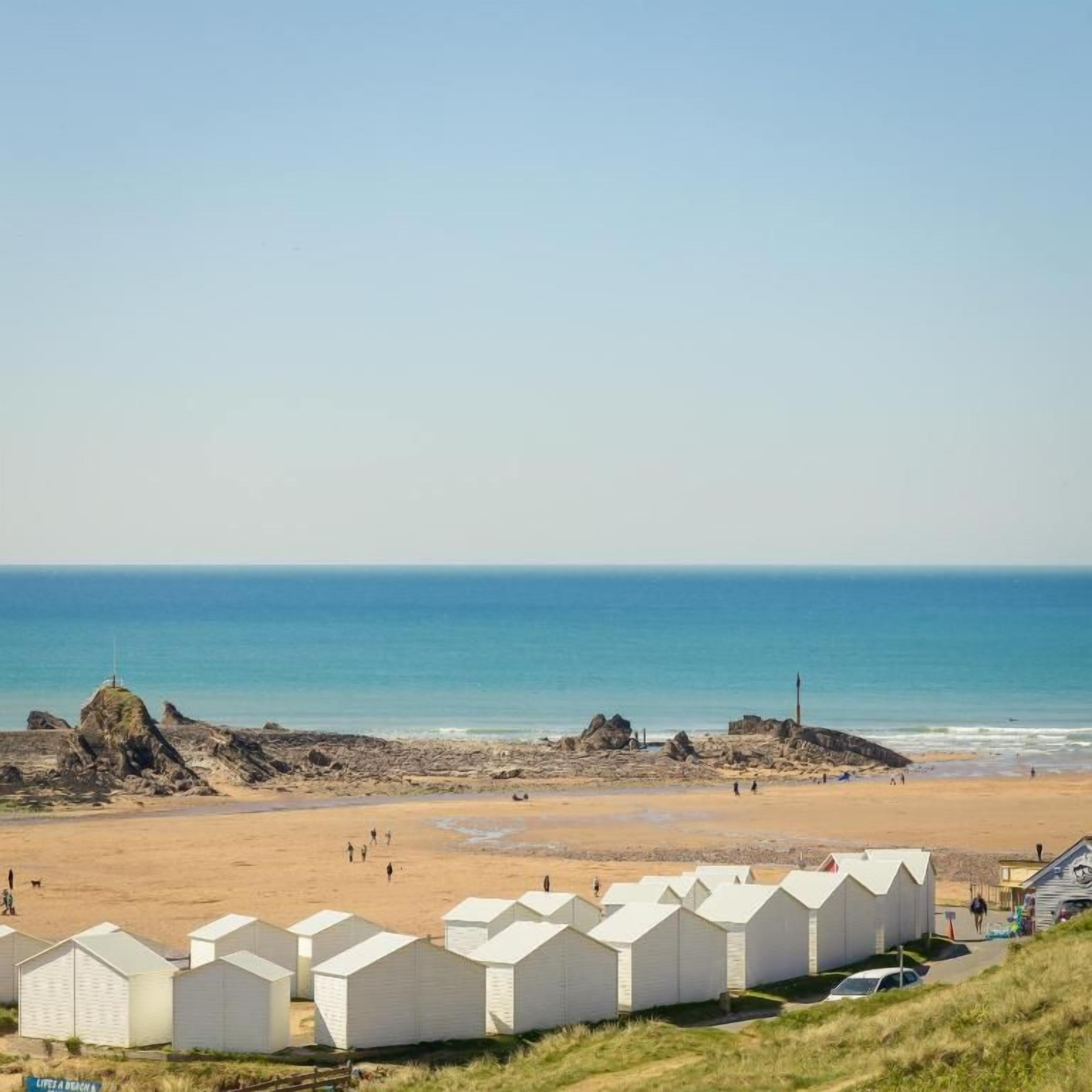 A beach with white beach huts and a clear view of the ocean.