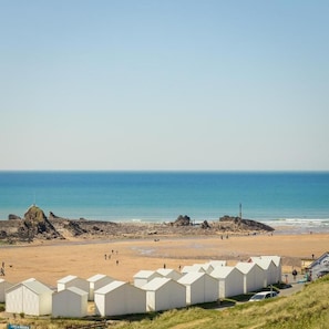 A beach with white beach huts and a clear view of the ocean. - The Edge Of The Beach (Bude)