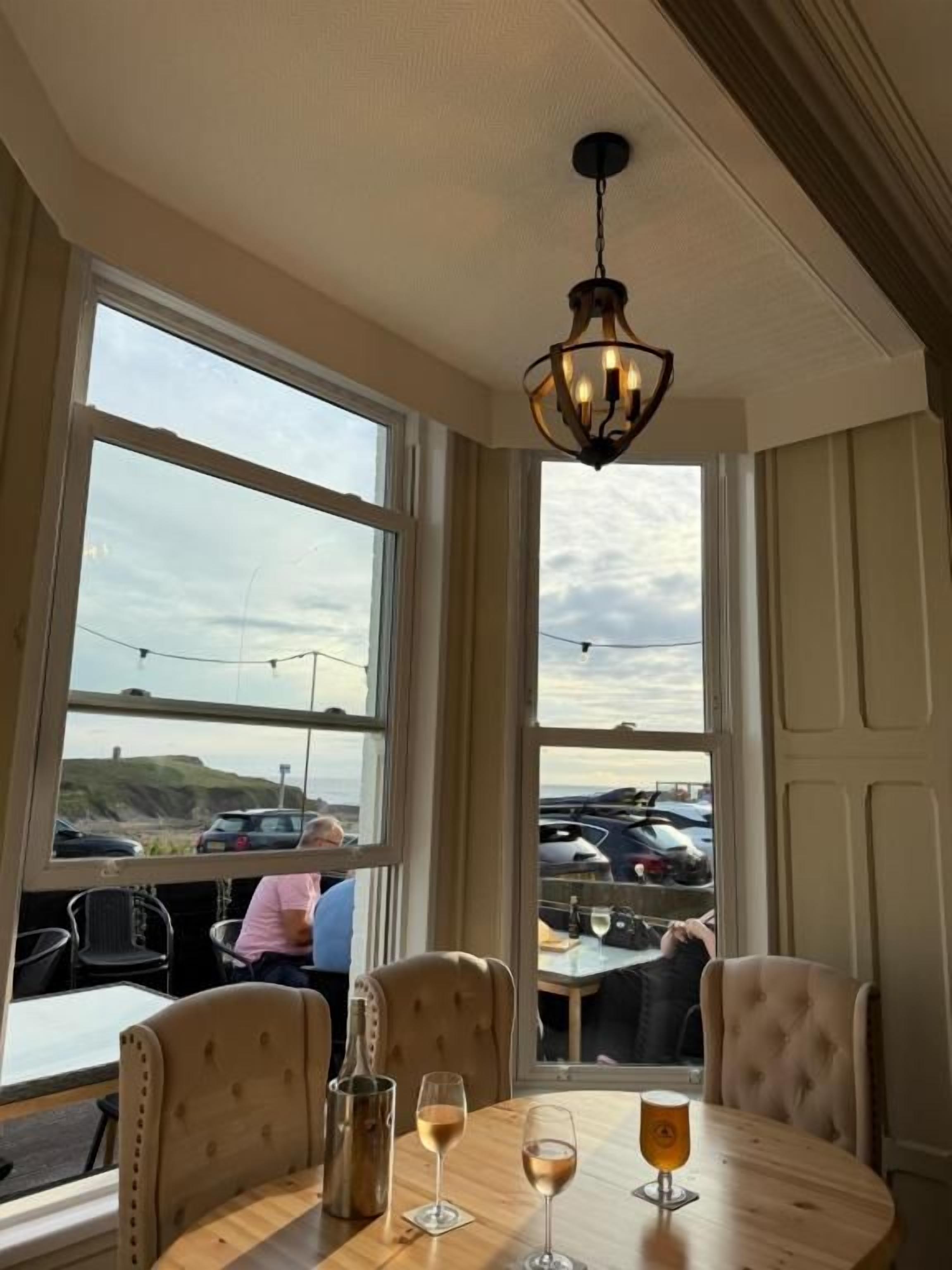 A dining area with a table set for two, large windows, and a hanging light fixture.