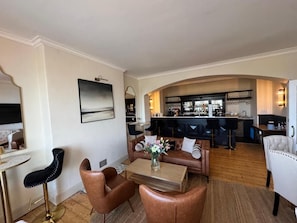 A modern living room with a sofa, coffee table, and a bar area in the background. - The Edge Of The Beach (Bude)