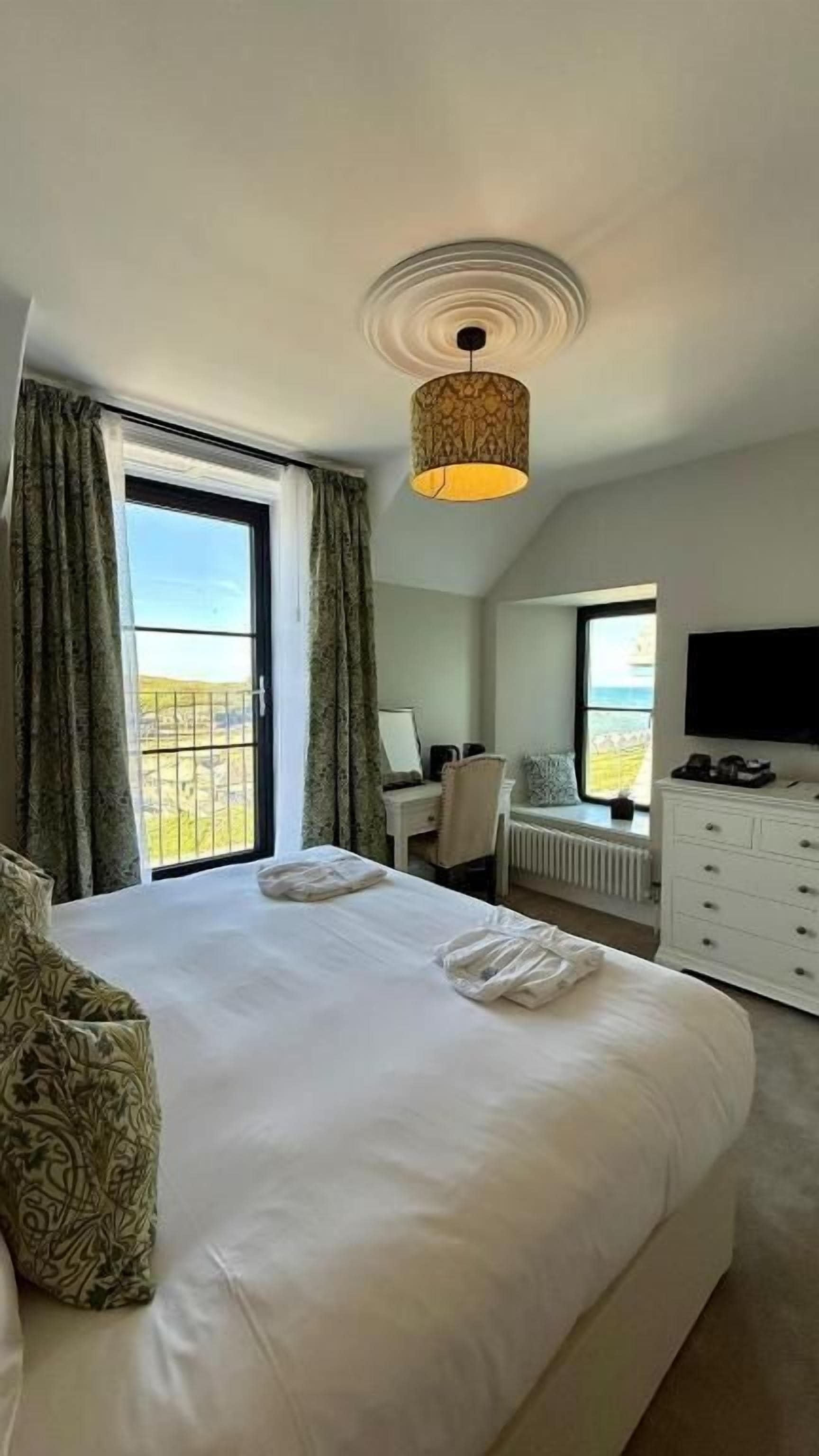 A hotel room with a large bed, a desk, a chair, a TV, and a view of the outdoors.