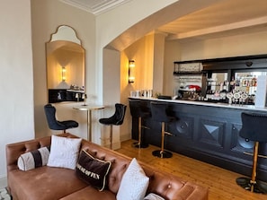 A bar area with stools, a counter with glasses, and a seating area with a couch and chairs.