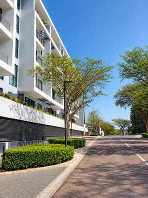 A modern building with balconies, a paved street, and greenery. - The Onyx Sandton Gate 2BR Luxury Stay. (Sandton)