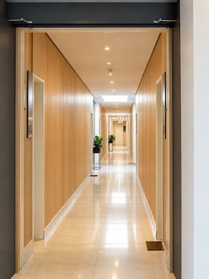 Passadís llarg i estret d'un hotel, amb revestiment de fusta a les parets, sòl de rajola i sostre amb il·luminació empotrada.