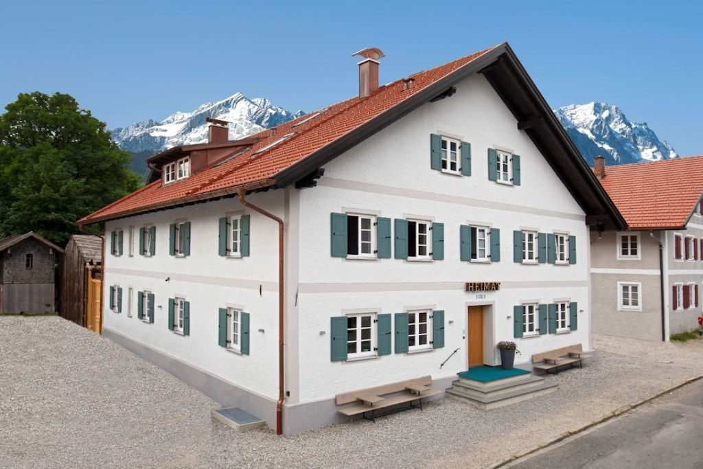 A two-story building with a sloped roof, multiple windows with shutters, and a small front porch with steps leading up to the entrance.