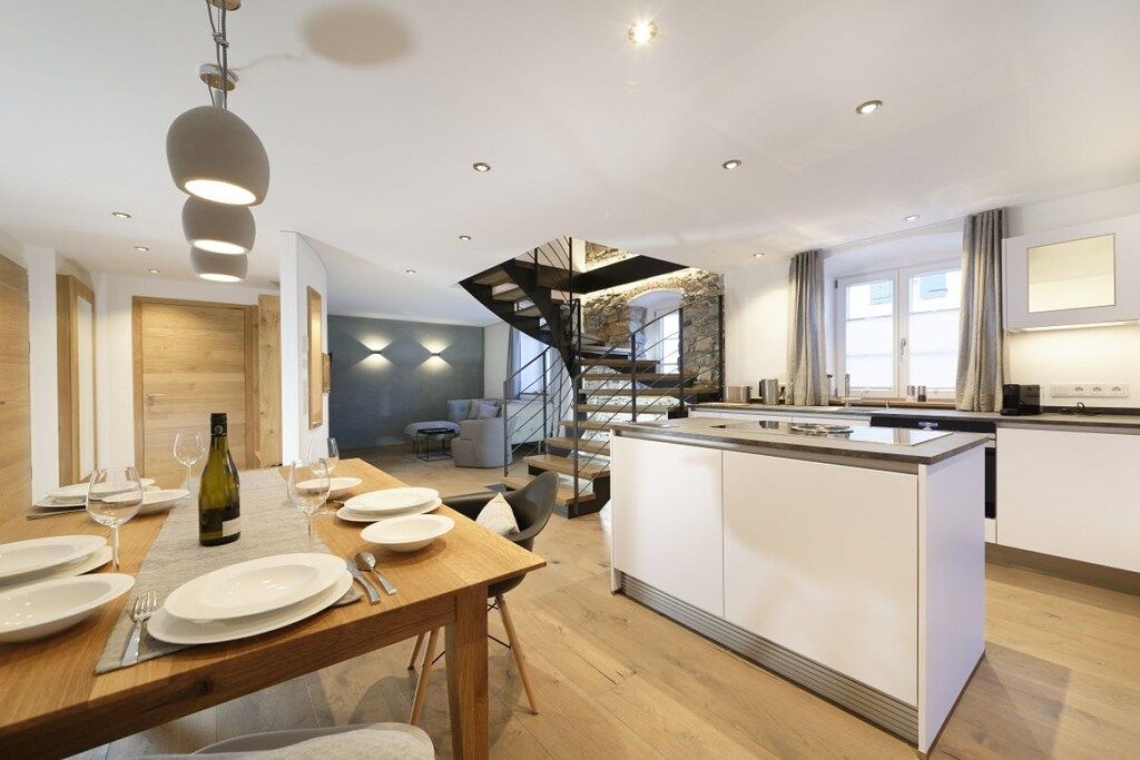 Une cuisine moderne dotée d’un îlot central, d’une table à manger en bois et d’un escalier menant à un niveau supérieur.