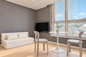 A modern living room with a white sofa, two white chairs, a round table, and a flat-screen TV mounted on the wall. - BLUEWING YACHT HOTEL (BUSAN)