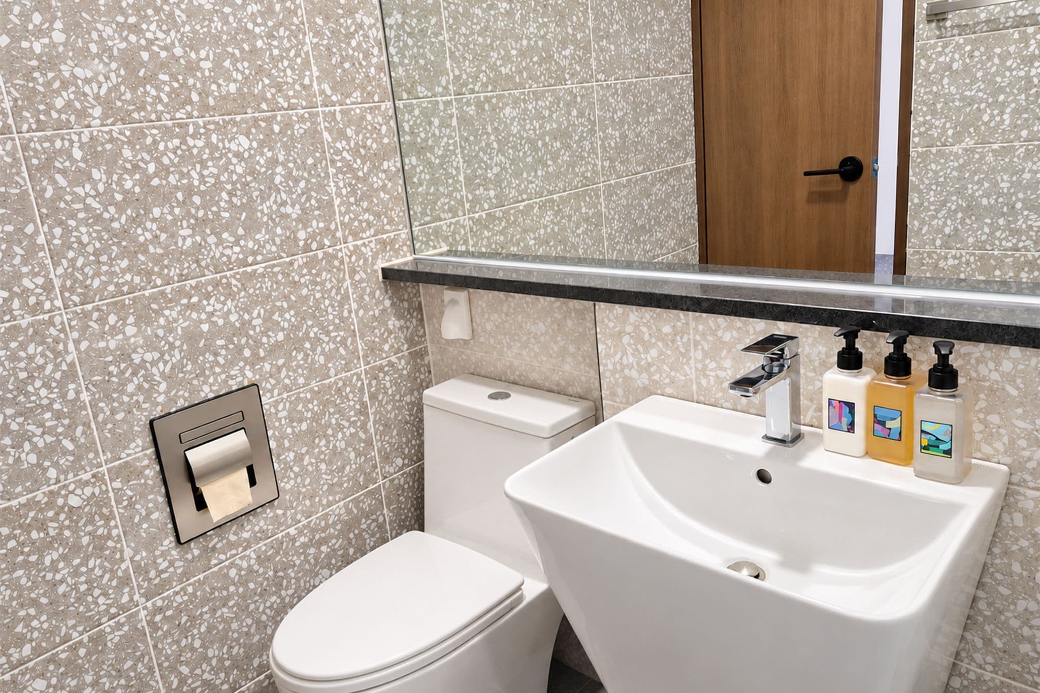 A bathroom with a toilet, sink, and hand soap dispensers.