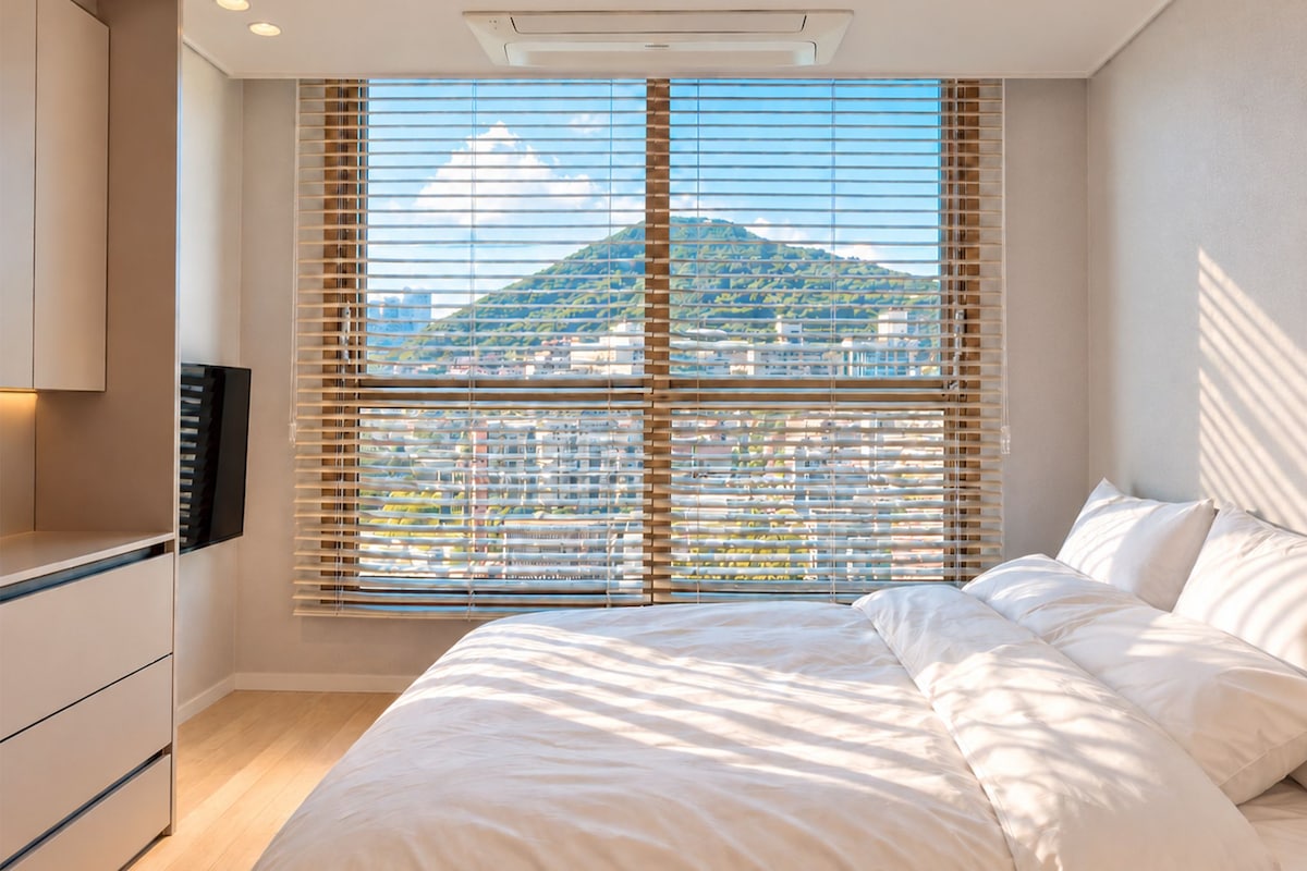 A bedroom with a bed, a TV, and a window with blinds.