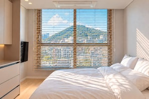 A bedroom with a bed, a TV, and a window with blinds. - BLUEWING YACHT HOTEL (BUSAN)