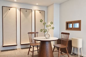 A dining area with a round table, four wooden chairs, a vase with green leaves, and three large wall panels. - BLUEWING YACHT HOTEL (BUSAN)