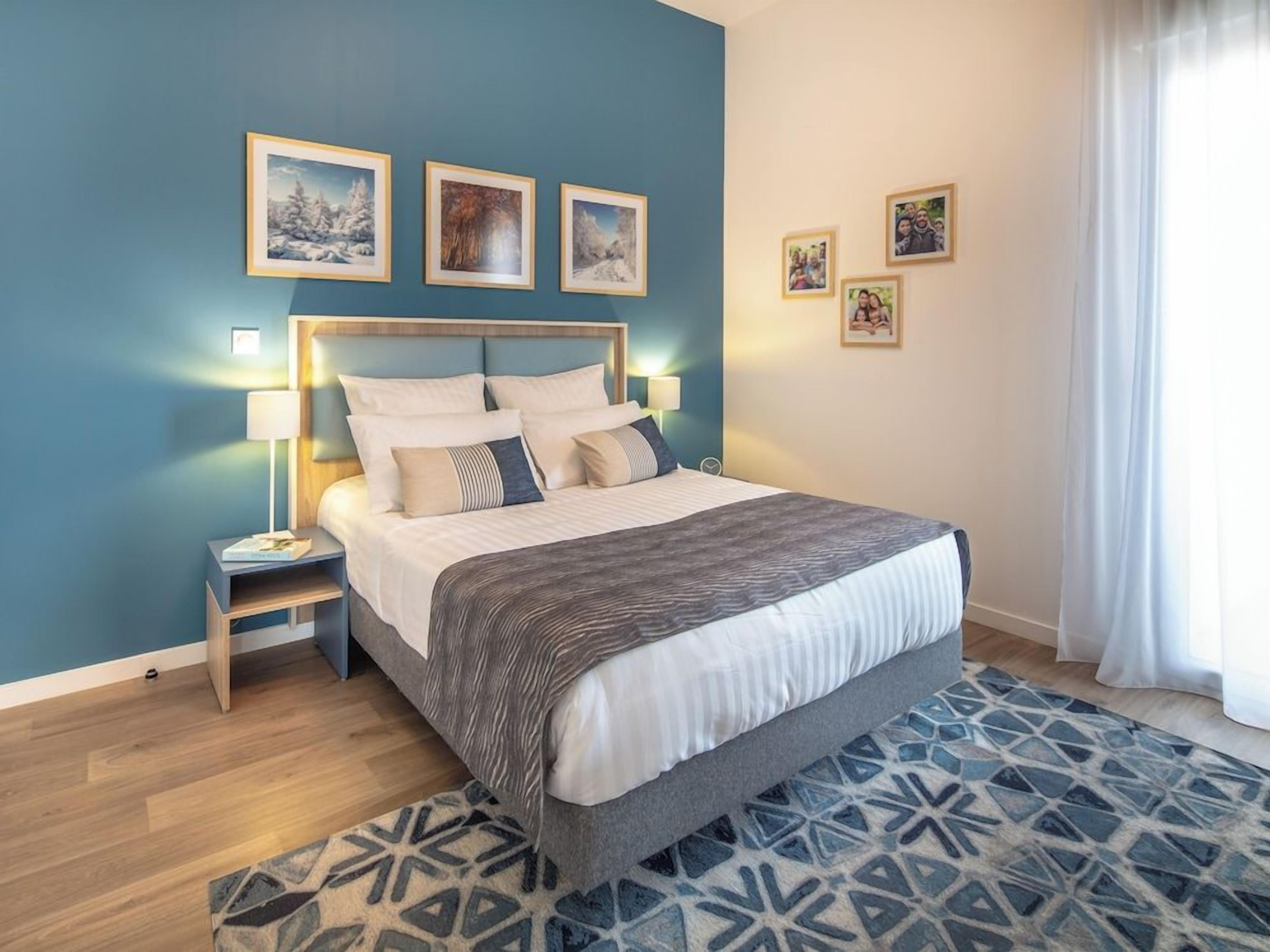 Quarto com cama, abajures, tapete estampado e quadros nas paredes.