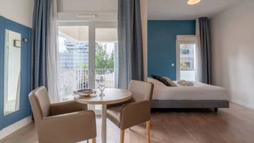 Una habitación de hotel moderna con una cama, una mesa redonda con sillas y un balcón con cortinas.