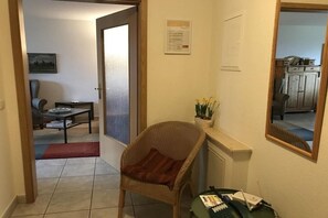 Ein Flur mit einem Korbstuhl, einem kleinen Tisch und einem Spiegel an der Wand.