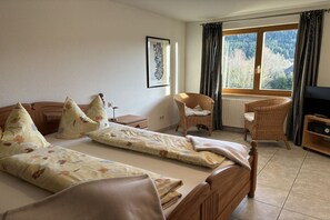 A room with two beds, a chair, a television, and a window with a view of trees. - Haus Seebachtal - Apartment 6 (Titisee)
