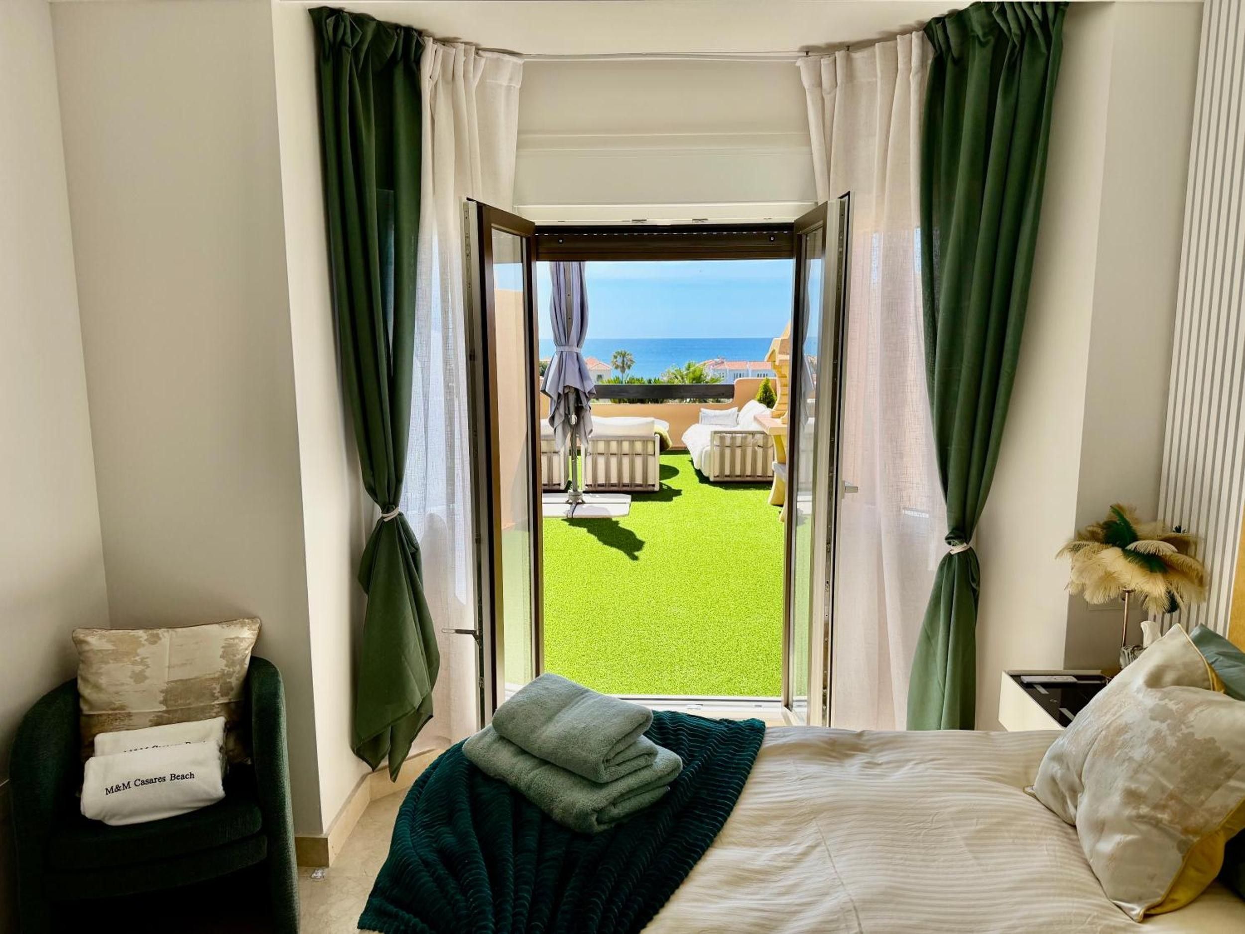 Una camera da letto con un letto, un comodino, una sedia e vista su un prato verde e un'area salotto all'aperto.