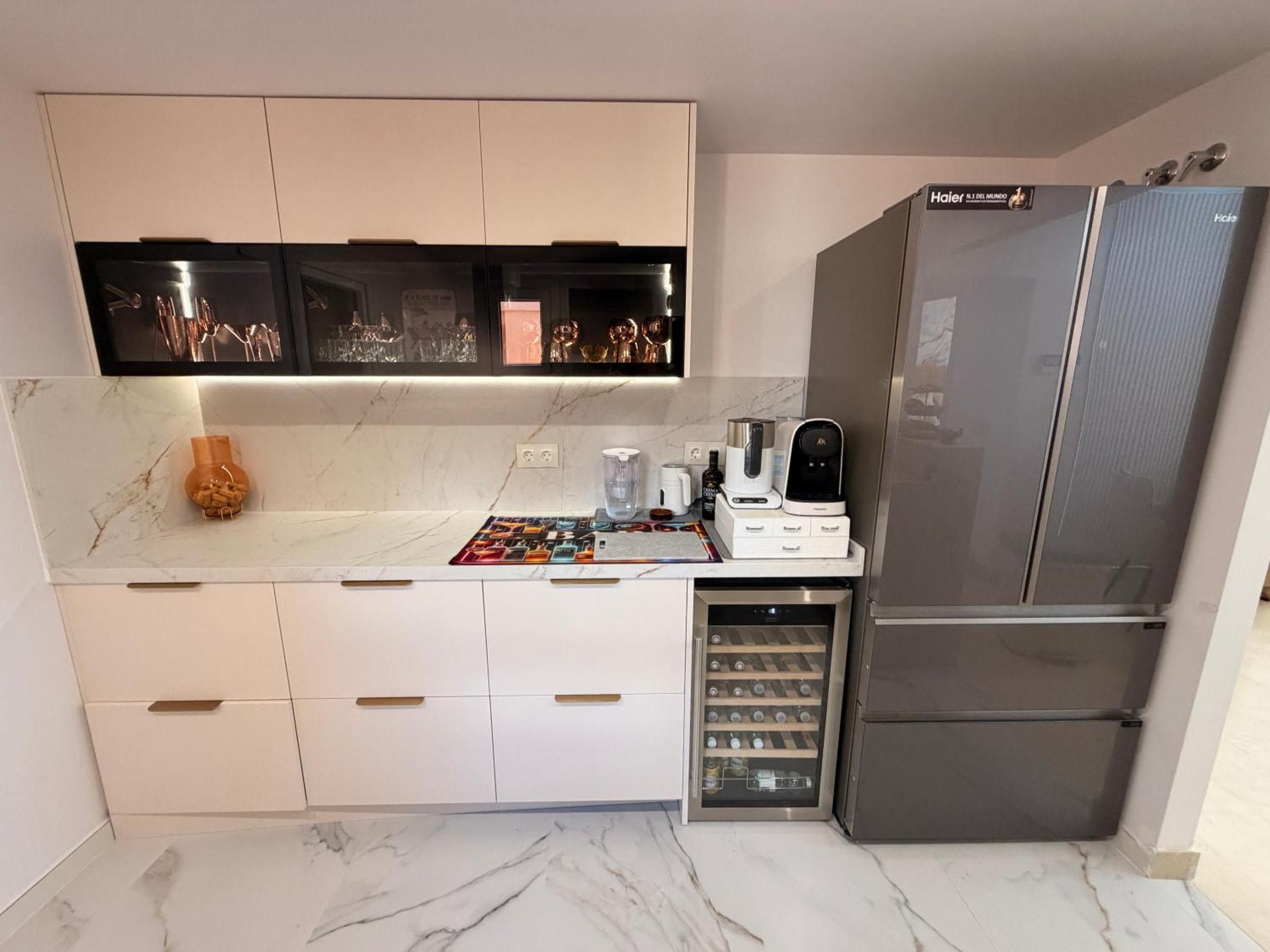 Una cucina moderna con un mini-frigo per il vino, un frigorifero in acciaio inox e un piano di lavoro in marmo.
