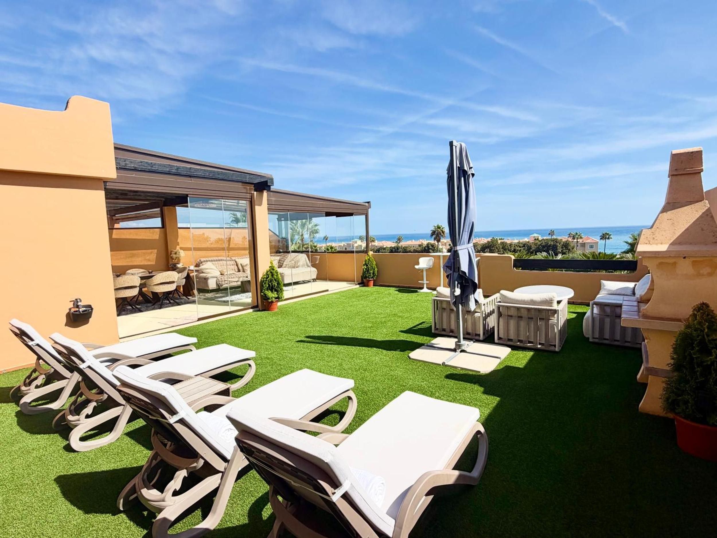 Eine Dachterrasse mit künstlichem Gras, Liegestühlen, Grillplatz und Blick auf den Ozean.