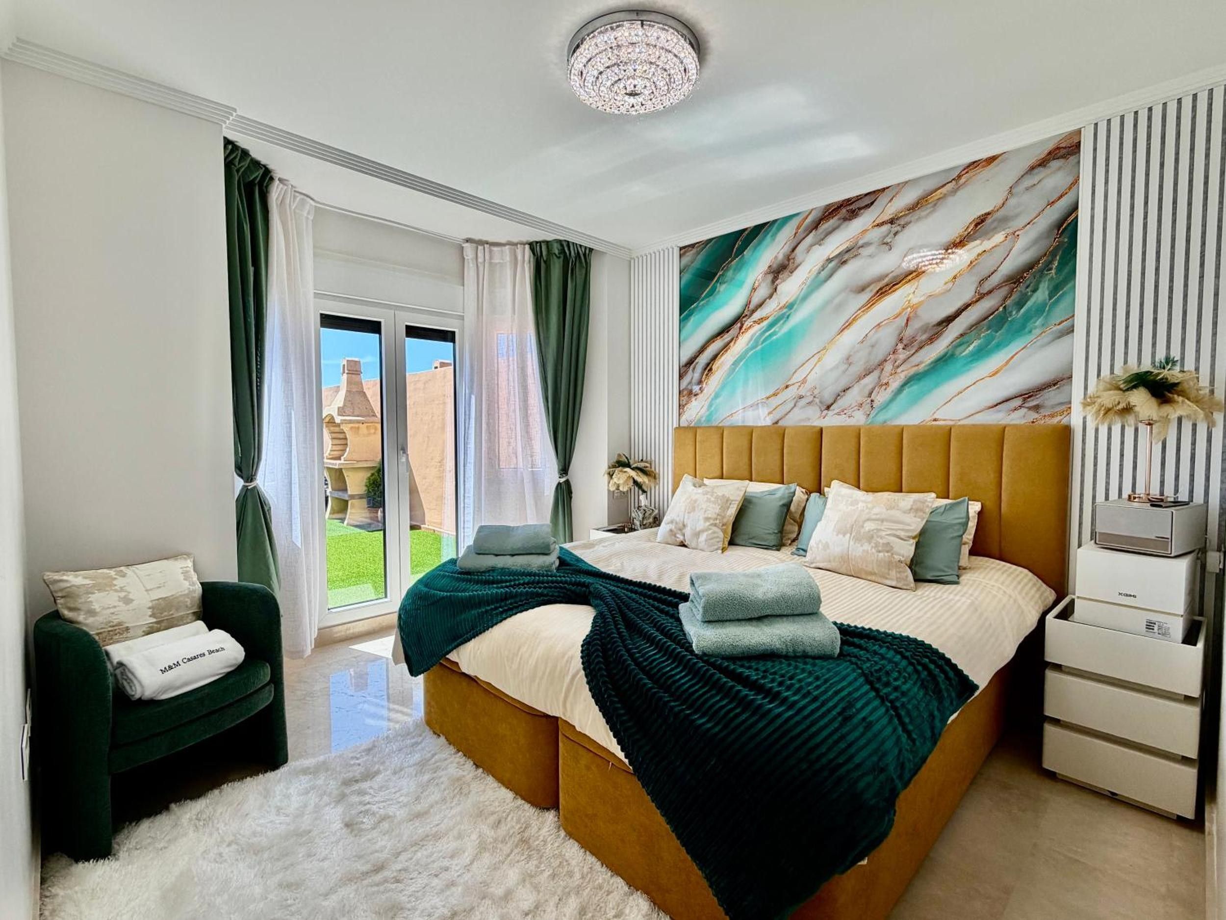 Een moderne slaapkamer met een groot bed, een groene fauteuil, een zacht wit vloerkleed en uitzicht op het groen.