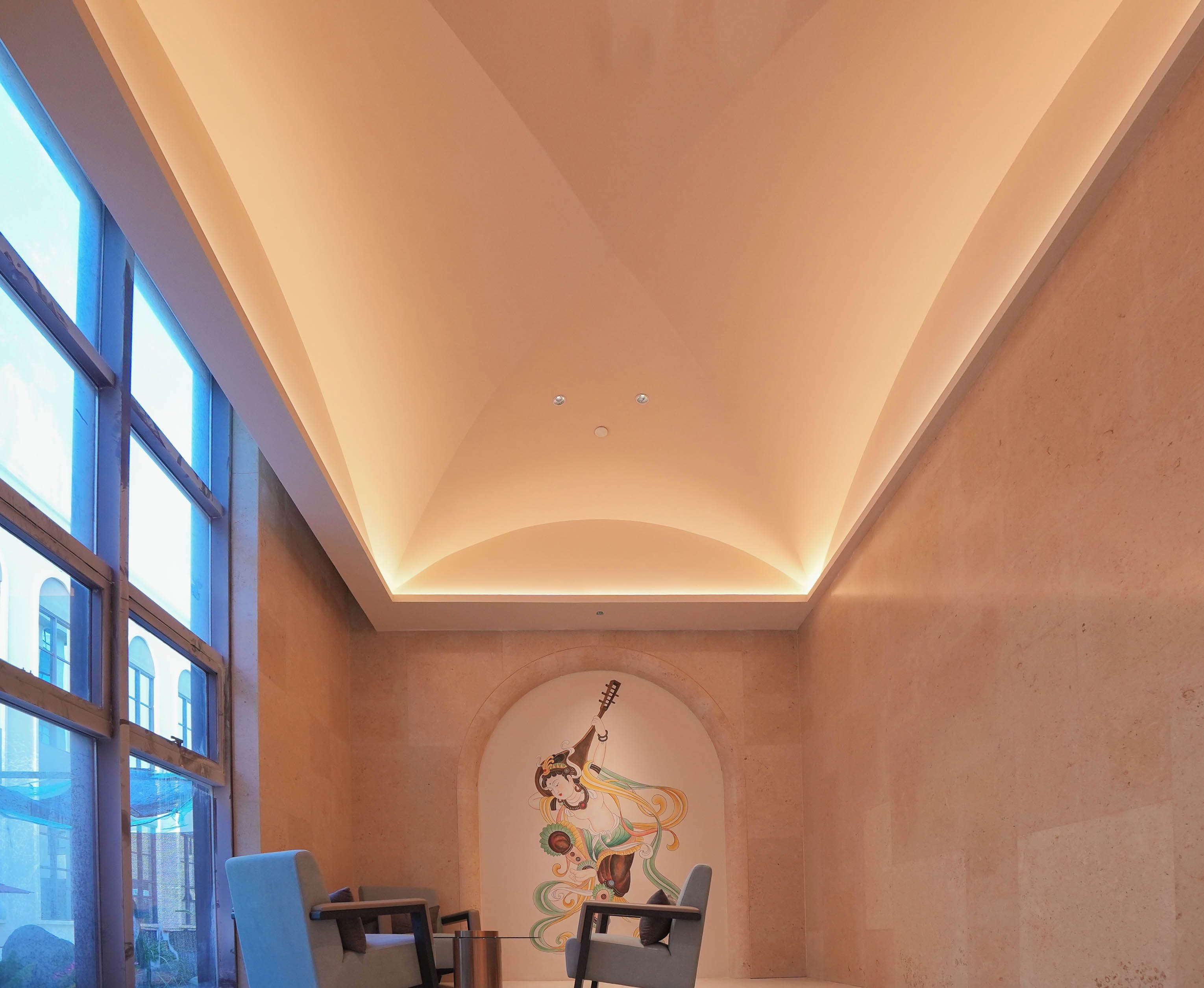 A room with a high ceiling, large windows, and a mural on the wall.