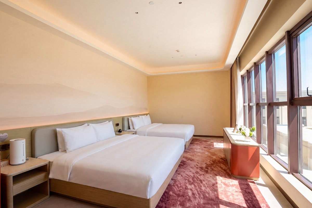 Habitación de hotel con dos camas, un escritorio, ventana con vistas y una pared de acento roja.