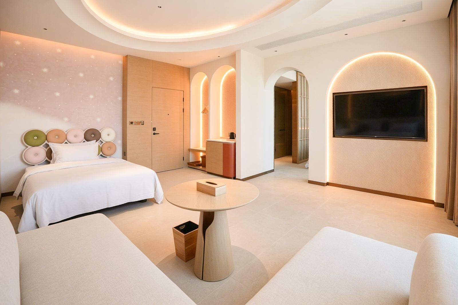Una habitación de hotel moderna con una cama, una mesa redonda, un televisor y un minibar.