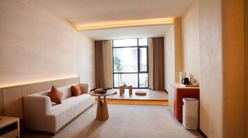 Habitación de hotel moderna con sofá, una mesita redonda, estación de café y vistas por una ventana grande.