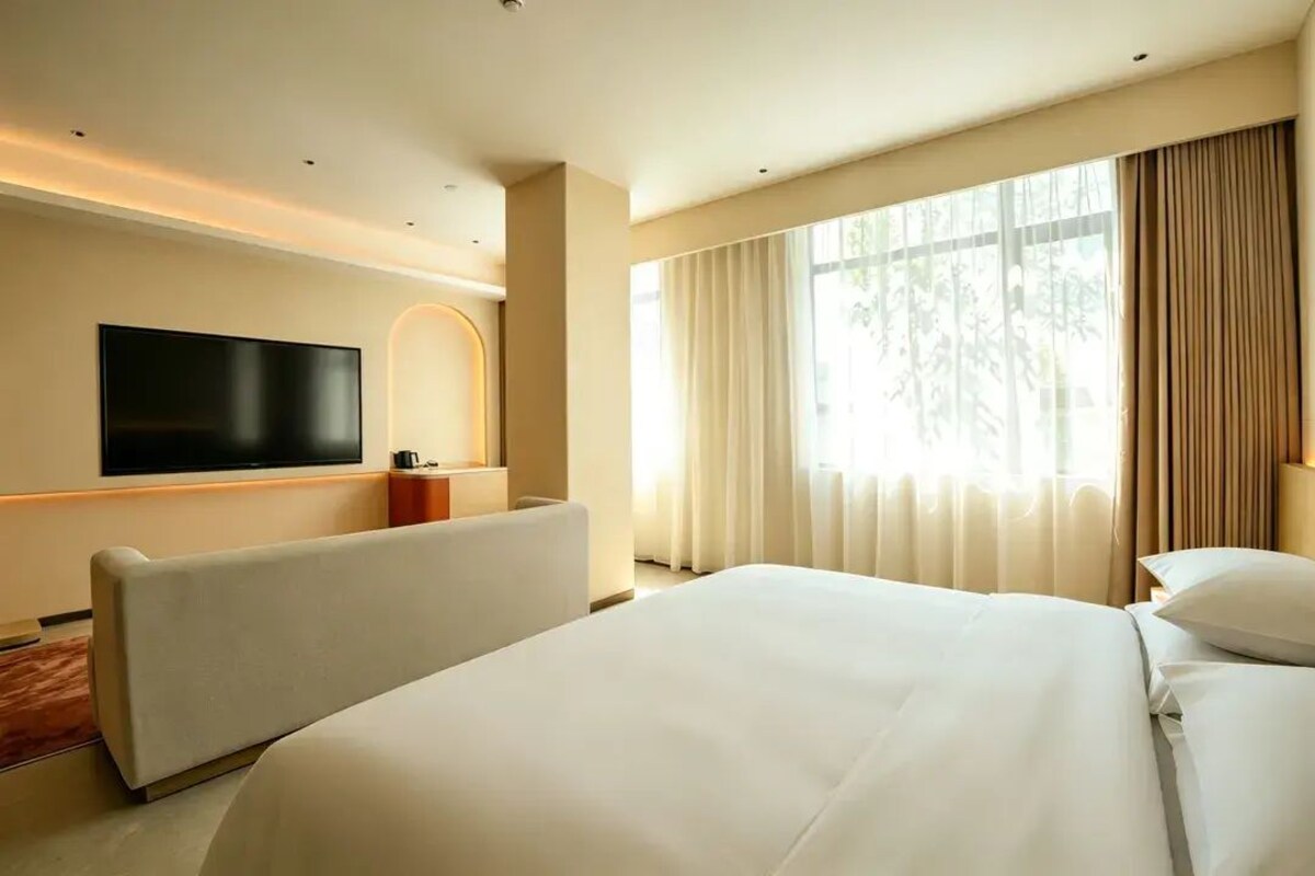 Habitación de hotel con una cama grande, televisor de pantalla plana en la pared, zona de estar y un amplio ventanal con cortinas.
