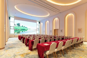 Un salón de conferencias con una mesa larga, sillas y una pantalla que muestra una vista panorámica.