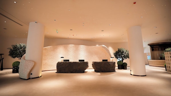 A reception area with a large rock-like feature, two reception desks, and potted plants.