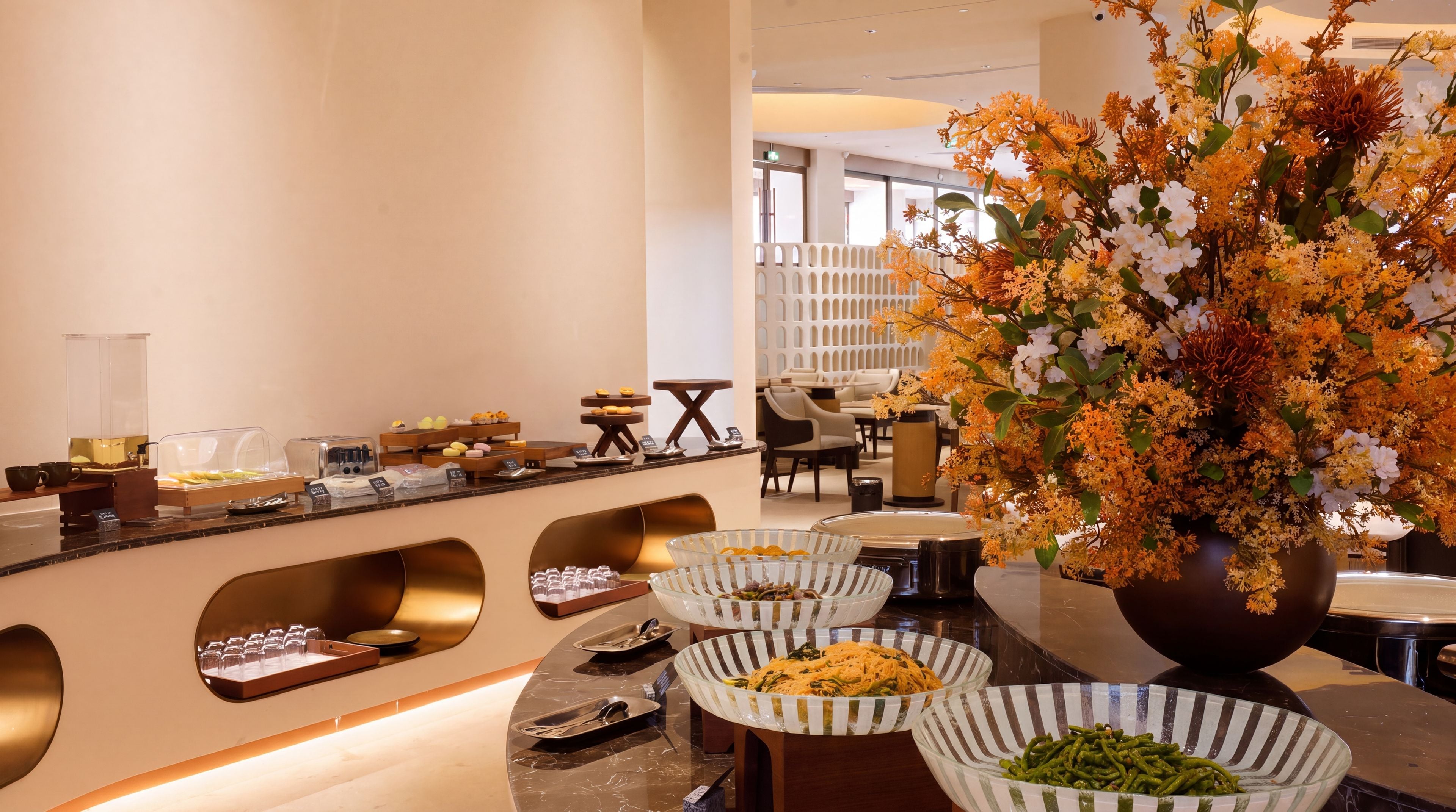 Un área de desayuno de hotel con bufé, mesas y una amplia decoración floral.