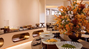 Un área de desayuno de hotel con bufé, mesas y una amplia decoración floral.