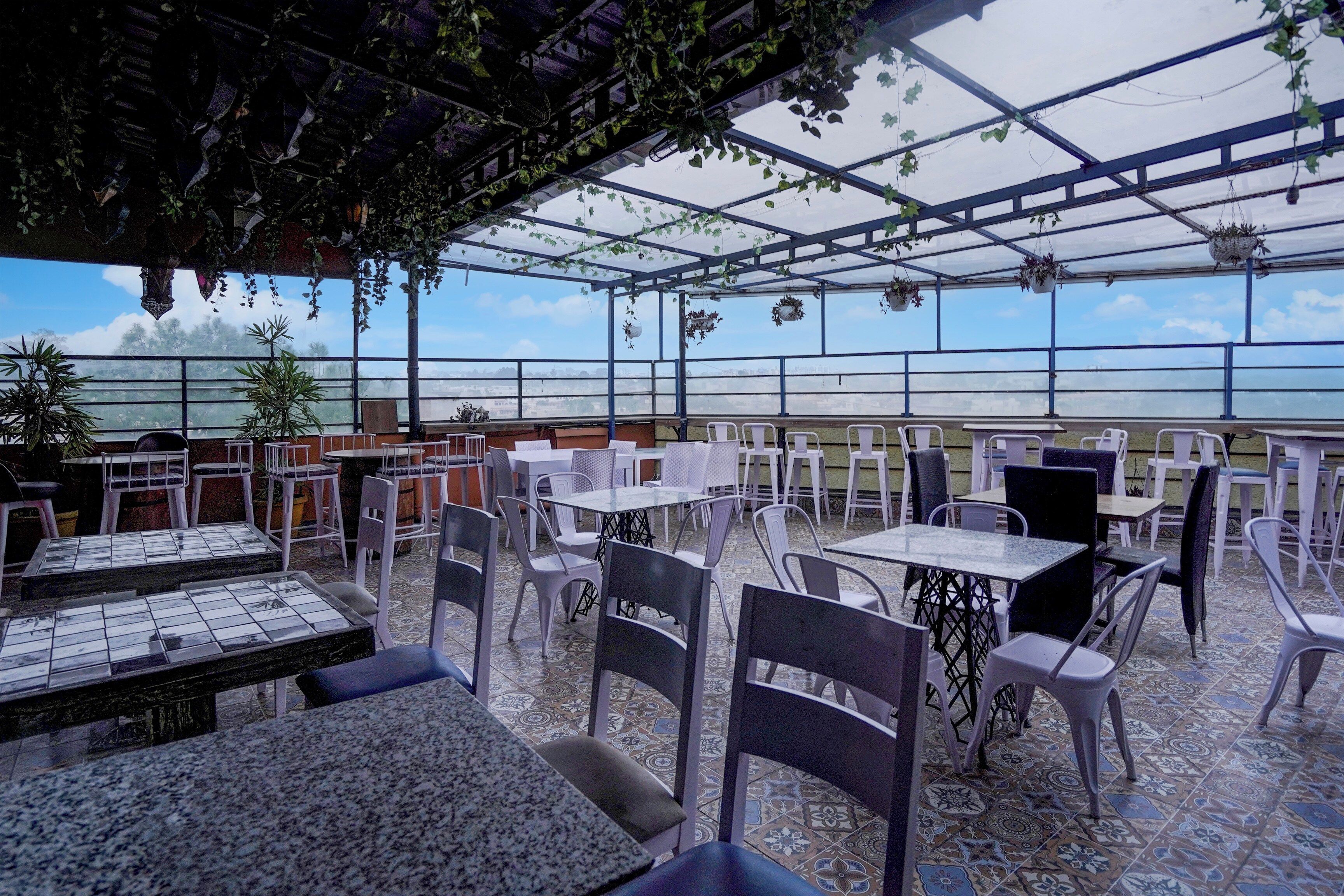 Café ao ar livre com mesas e cadeiras, vista para a cidade e plantas penduradas.