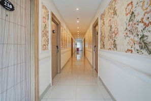 Un pasillo de hotel con puertas de madera, papel tapiz floral y suelo de baldosas.