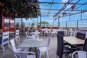 Un café al aire libre con mesas y sillas, una puerta roja y plantas colgantes.