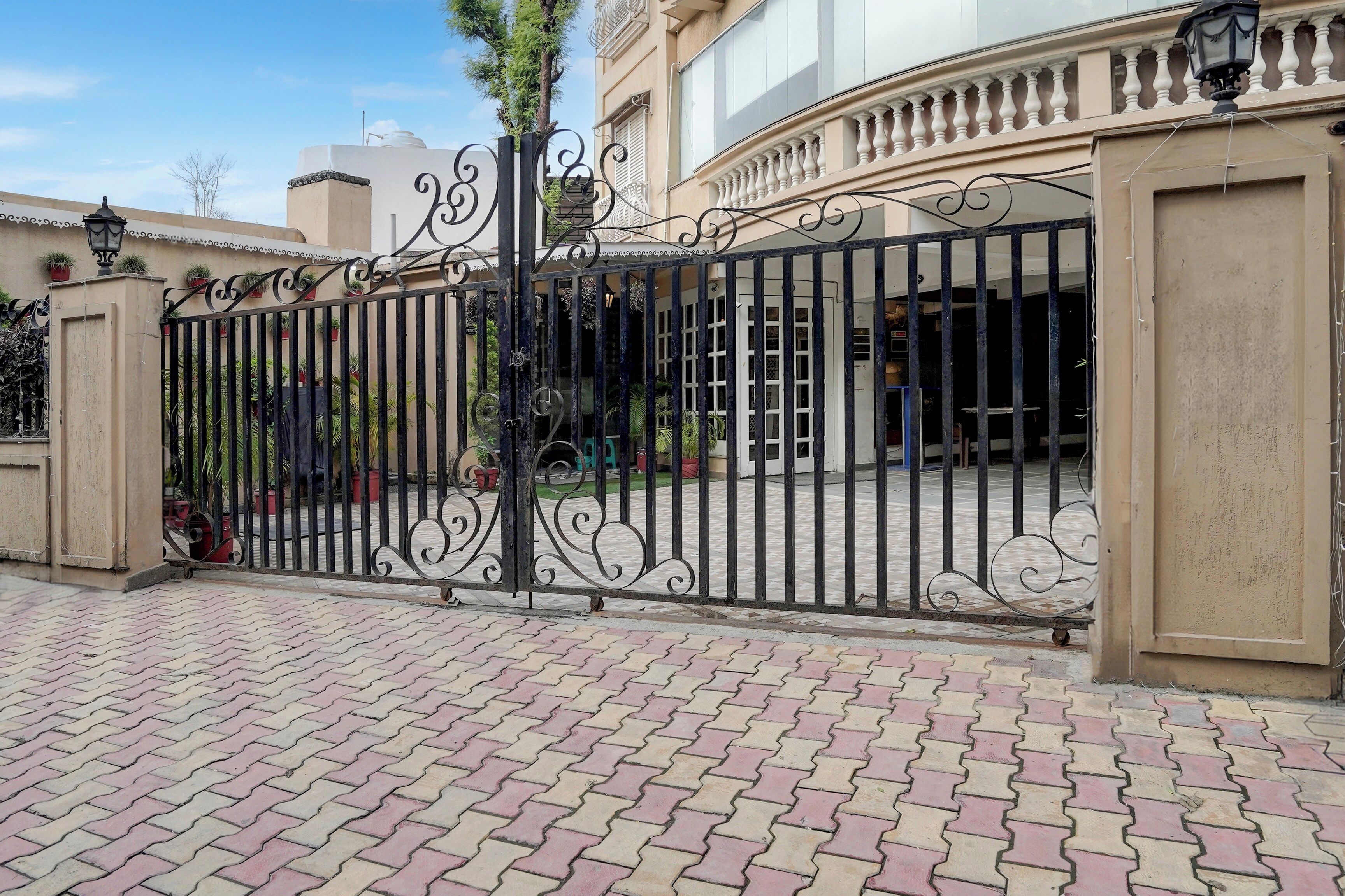 A gated entrance with a decorative iron gate, potted plants, and a paved walkway.